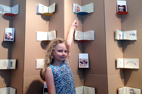 A young person points up to an installation of books mounted onto cardboard pillars