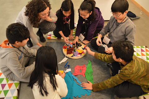 A group of young people and an adult circle around an art project on the floor of the ArtStarts Gallery