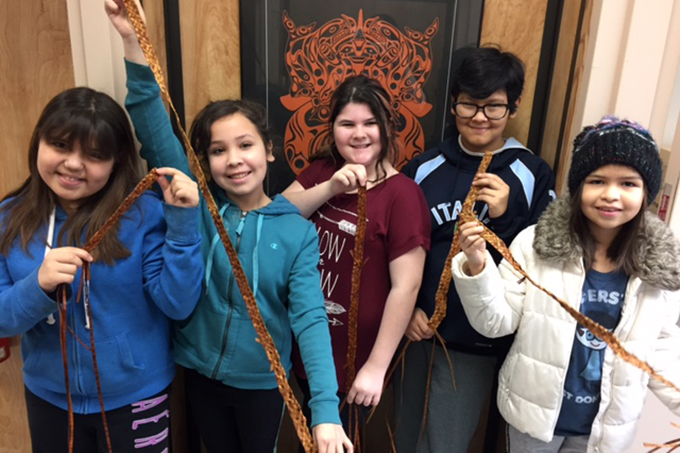 A group of young learners pose with woven belts