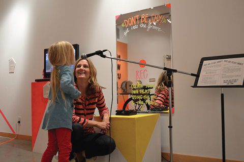 A small child singing into a microphone while an adult is crouched down next to them smiling