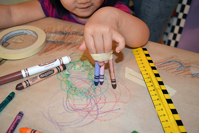 A young person drawing with 3 crayons taped to their finger