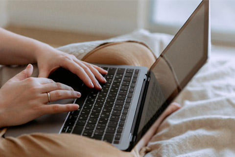 A person typing on a laptop resting on their lap