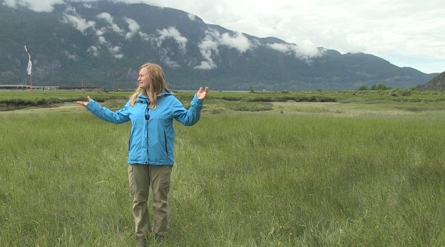 Rhonda O'grady of Squamish River Watershed Society stands in the valley with mountains in the background. Still from Herring: the heart of Squamish. A documentary created by students at St’a7mes School - Learning Expeditions and co-produced by The Cinematheque © 2021